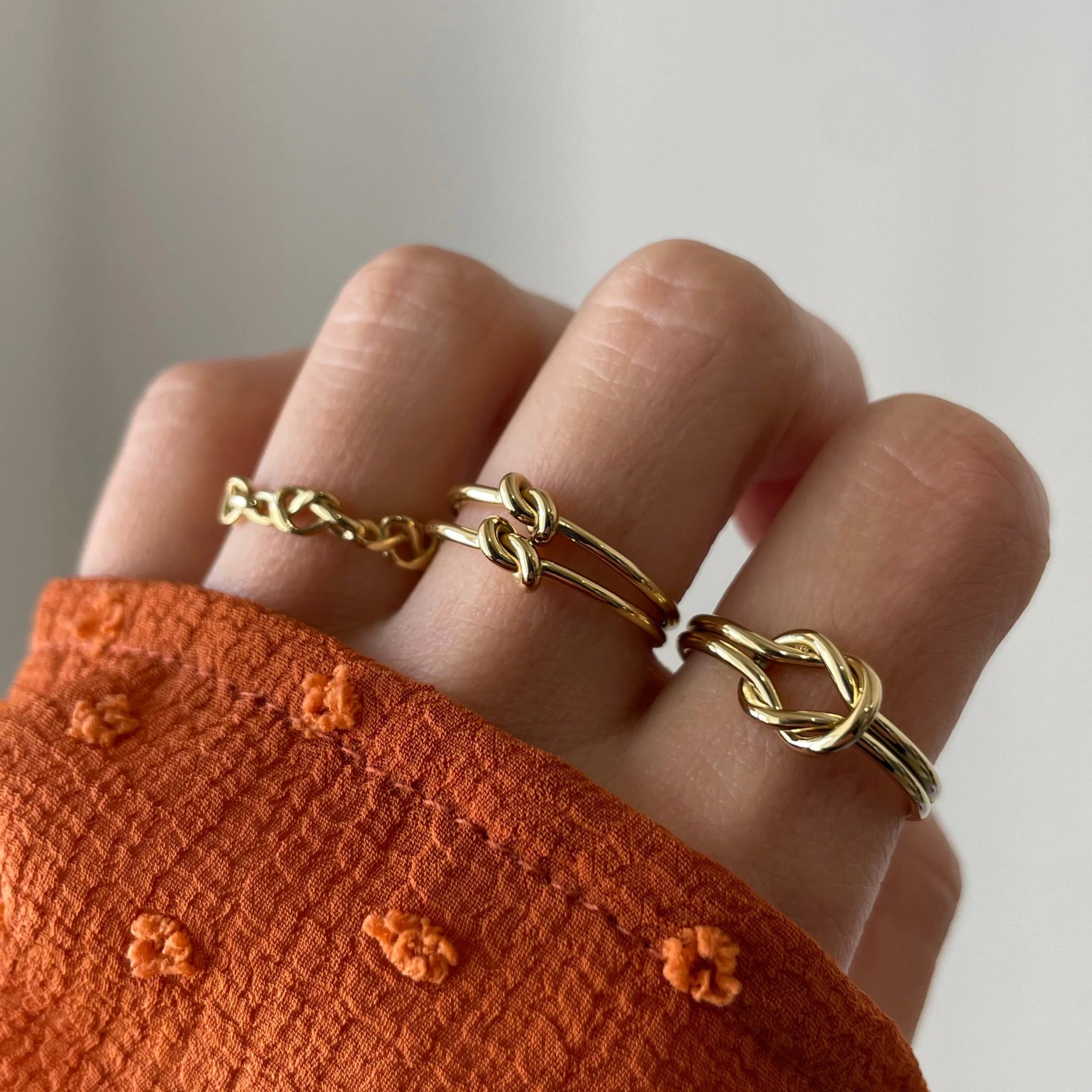 Bague Marina portée en accumulation (stacking) avec d'autres bagues fines dorées sur une main avec manche rouille.