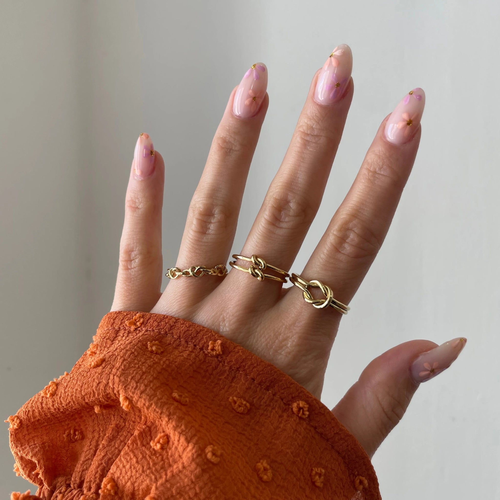 Bague Marina portée en accumulation (stacking) avec d'autres bagues fines dorées sur une main avec manche rouille.