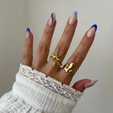 Bague organique Mattia portée en accumulation (stacking) avec une bague étoile de mer et d'autres bijoux dorés.