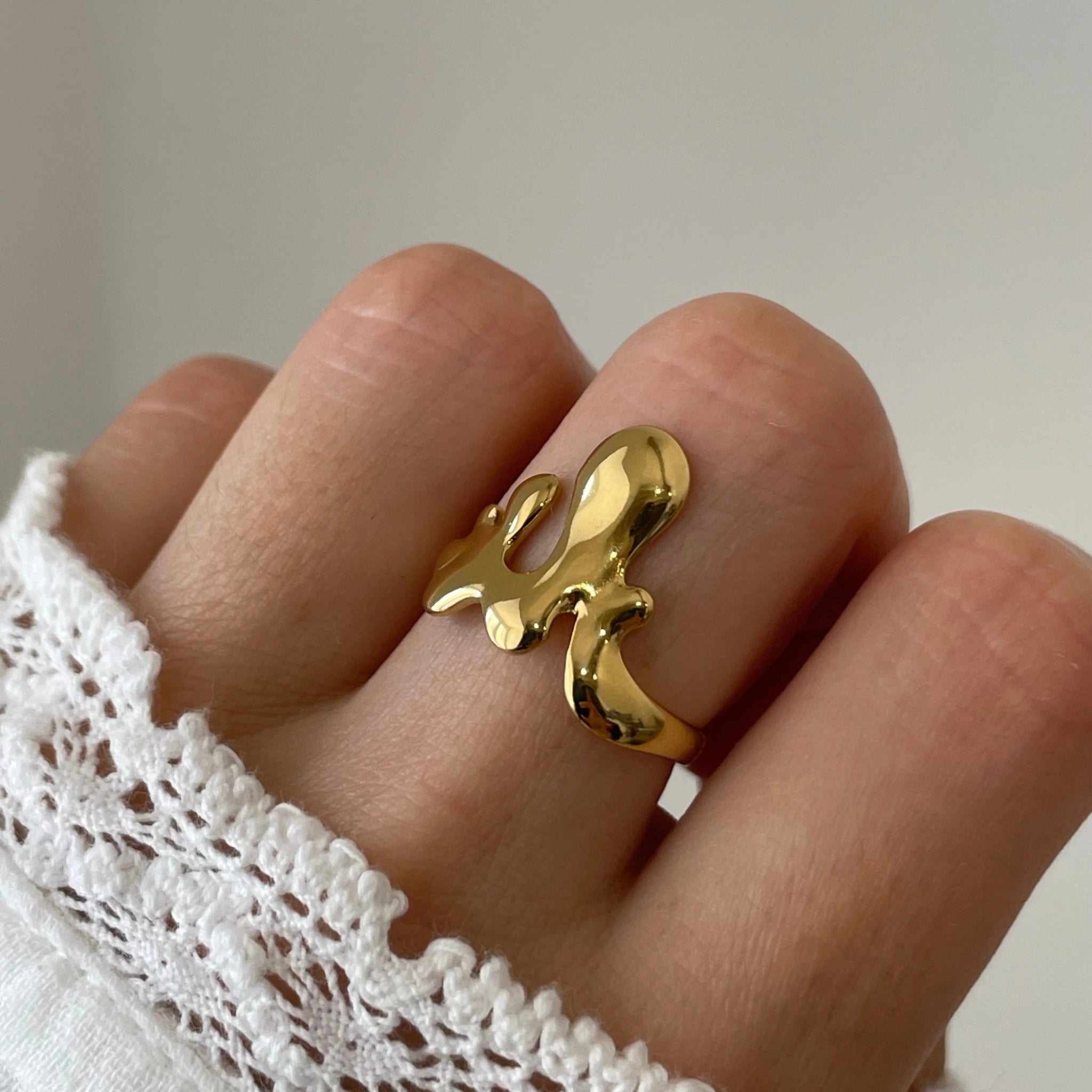 Gros plan bague Mattia style métal fondu ou gouttes d'eau fluides portée au doigt, design artistique et moderne.