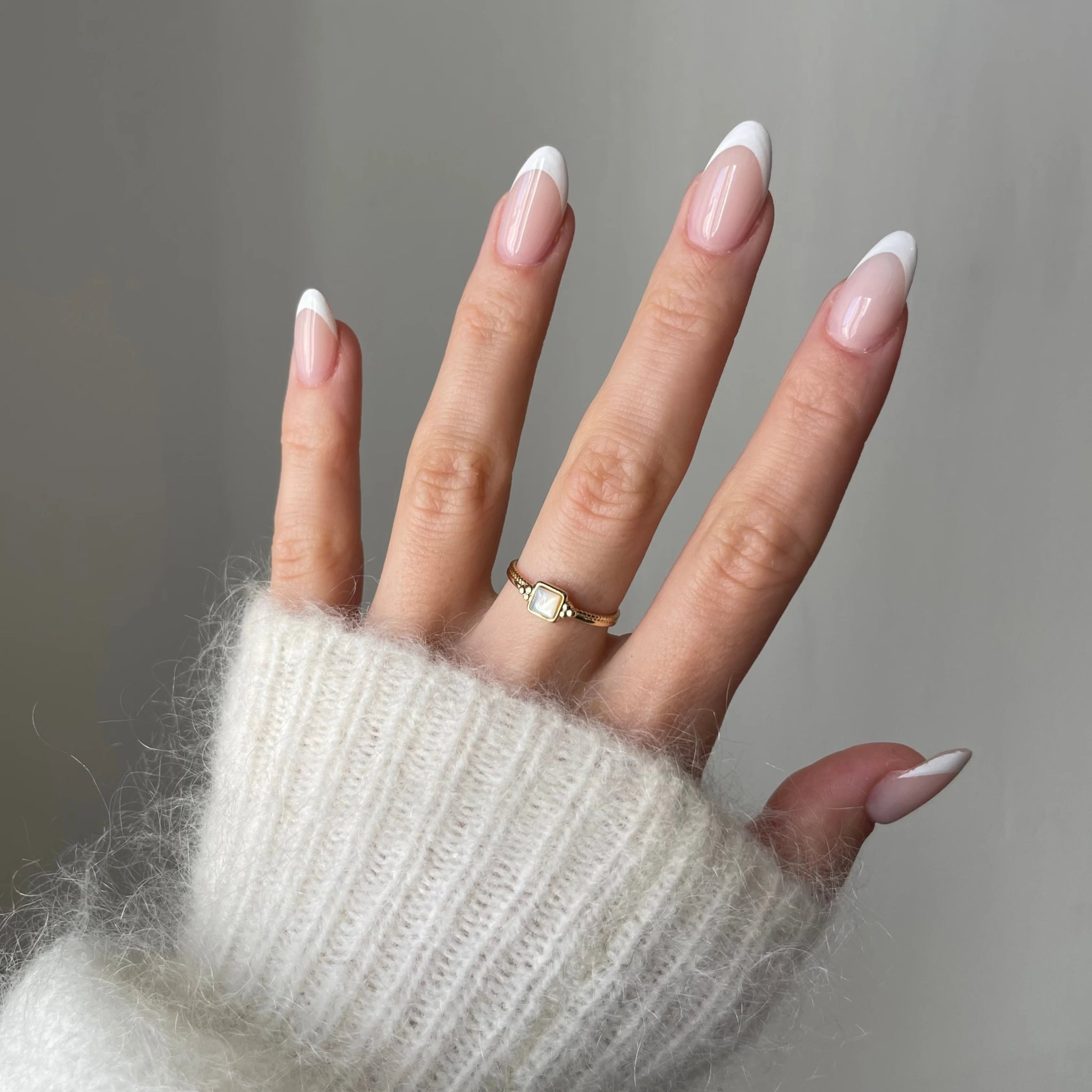 Bague fine Melania portée en accumulation (stacking) avec d'autres bagues dorées et perles sur une main manucurée.