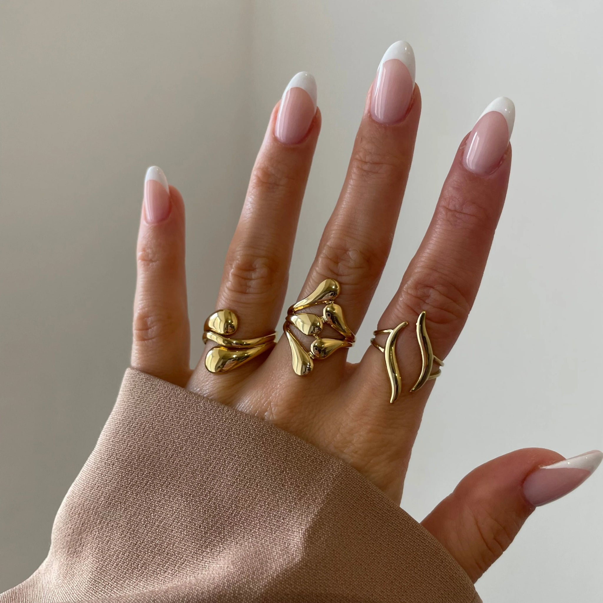 Bague Mina portée en accumulation (stacking) avec d'autres bagues graphiques dorées sur une main.