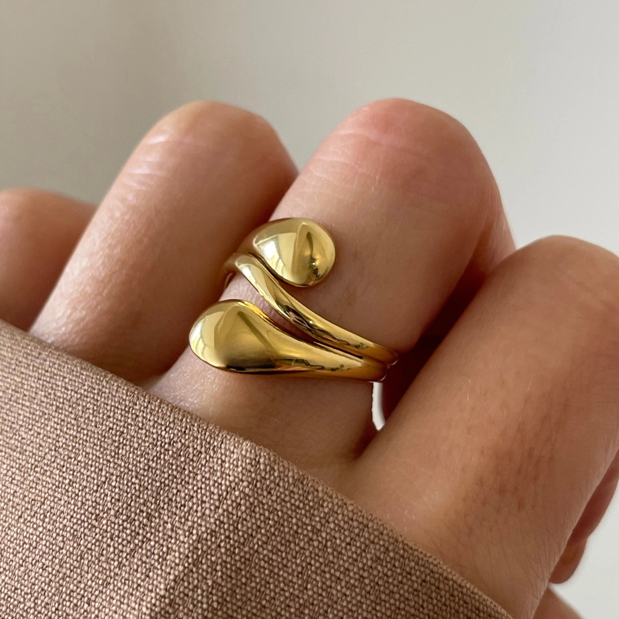 Gros plan bague Mina forme gouttes d'eau fluides portée au doigt, design moderne.