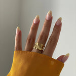 Bague statement large et dorée portée au doigt, accessoire mode tendance.