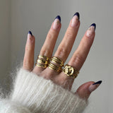 Bague épaisse dorée style surface irrégulière portée sur une main manucurée.