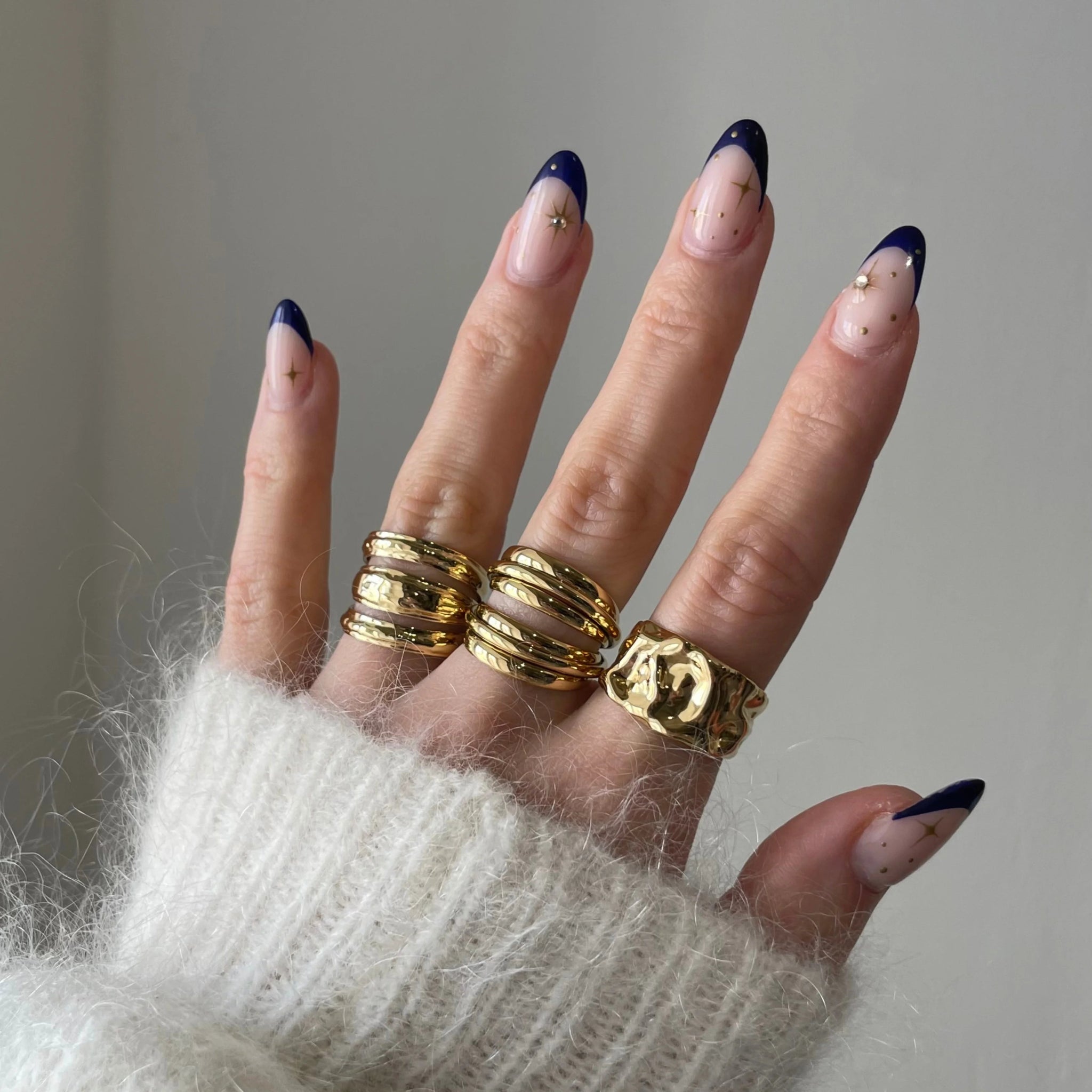 Bague épaisse dorée style surface irrégulière portée sur une main manucurée.