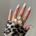 Bague dorée 3 motifs nacre: 1 ovale, 2 ronds à bord perlé, sur main femme aux ongles blancs. Manchette léopard plissée.