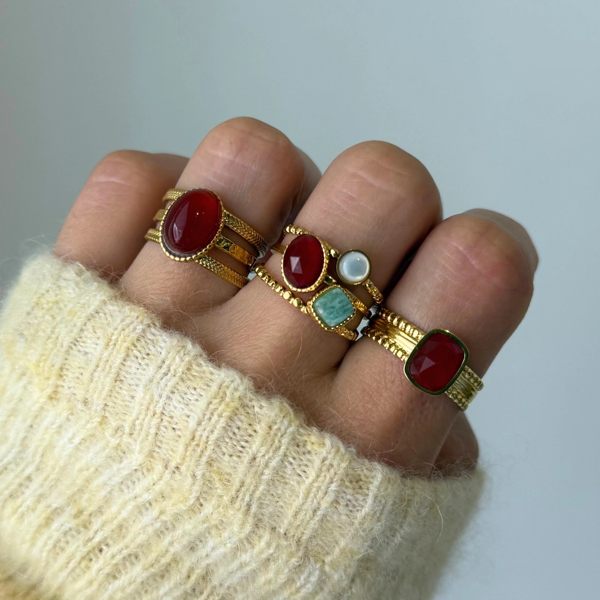 Bague Mylena rouge portée en accumulation (stacking) avec d'autres bagues à pierres colorées (turquoise, blanc).