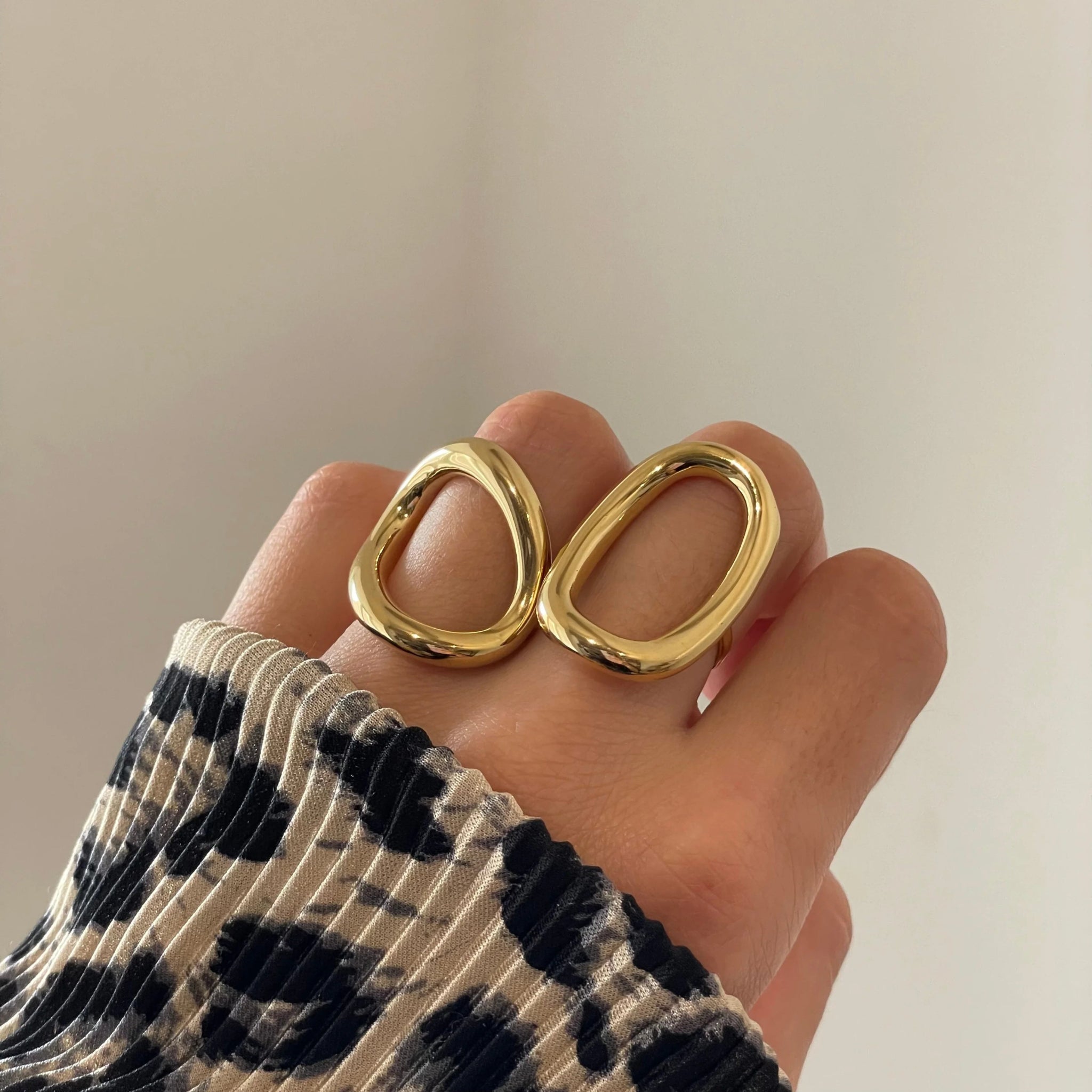Bague graphique Anastasia portée en accumulation avec d'autres bagues dorées sur une main avec pull léopard.
