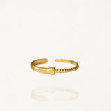 Bague fine ouverte en acier inoxydable doré avec détail texturé effet strié ou bobine sur fond blanc.