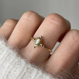 Gros plan bague Rosaria dorée avec pierre aspect nacre portée au doigt, style délicat et bohème.