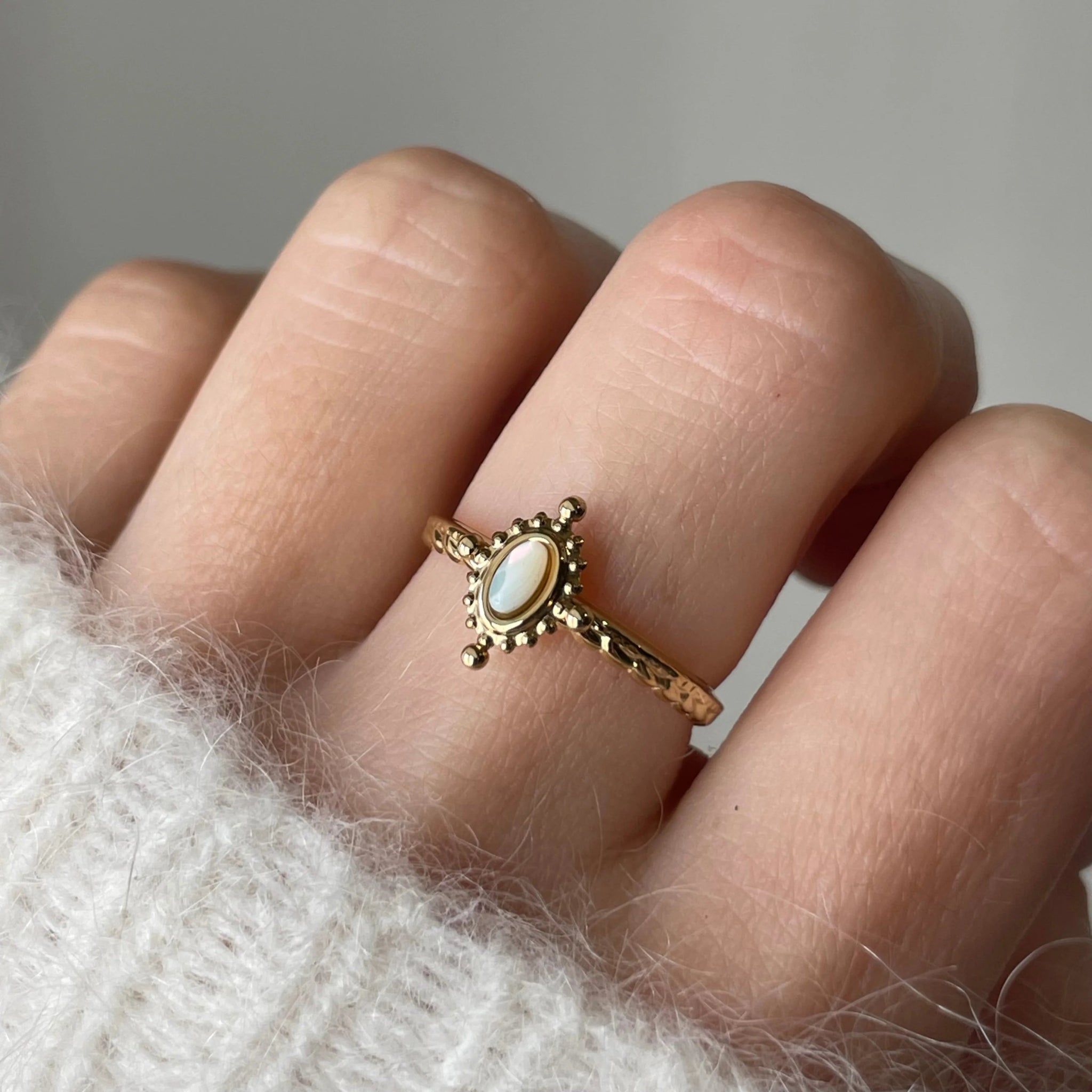 Gros plan bague Rosaria dorée avec pierre aspect nacre portée au doigt, style délicat et bohème.