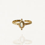 Bague fine ajustable en acier inoxydable doré avec petite pierre ovale blanche et contour perlé style vintage sur fond blanc."