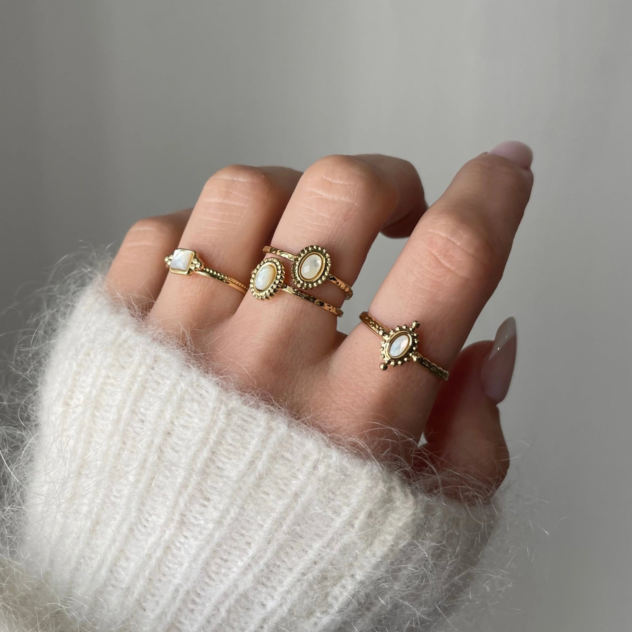 Bague Rosaria portée en accumulation (stacking) avec d'autres bagues fines dorées et pierres blanches sur une main.