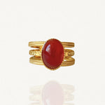 Bague large multi-rangs en acier inoxydable doré ornée d'une pierre ovale rouge rubis (style cornaline) sur fond blanc.