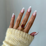 Bague Rubia style vintage avec pierre rouge portée sur une main avec manche en maille jaune.