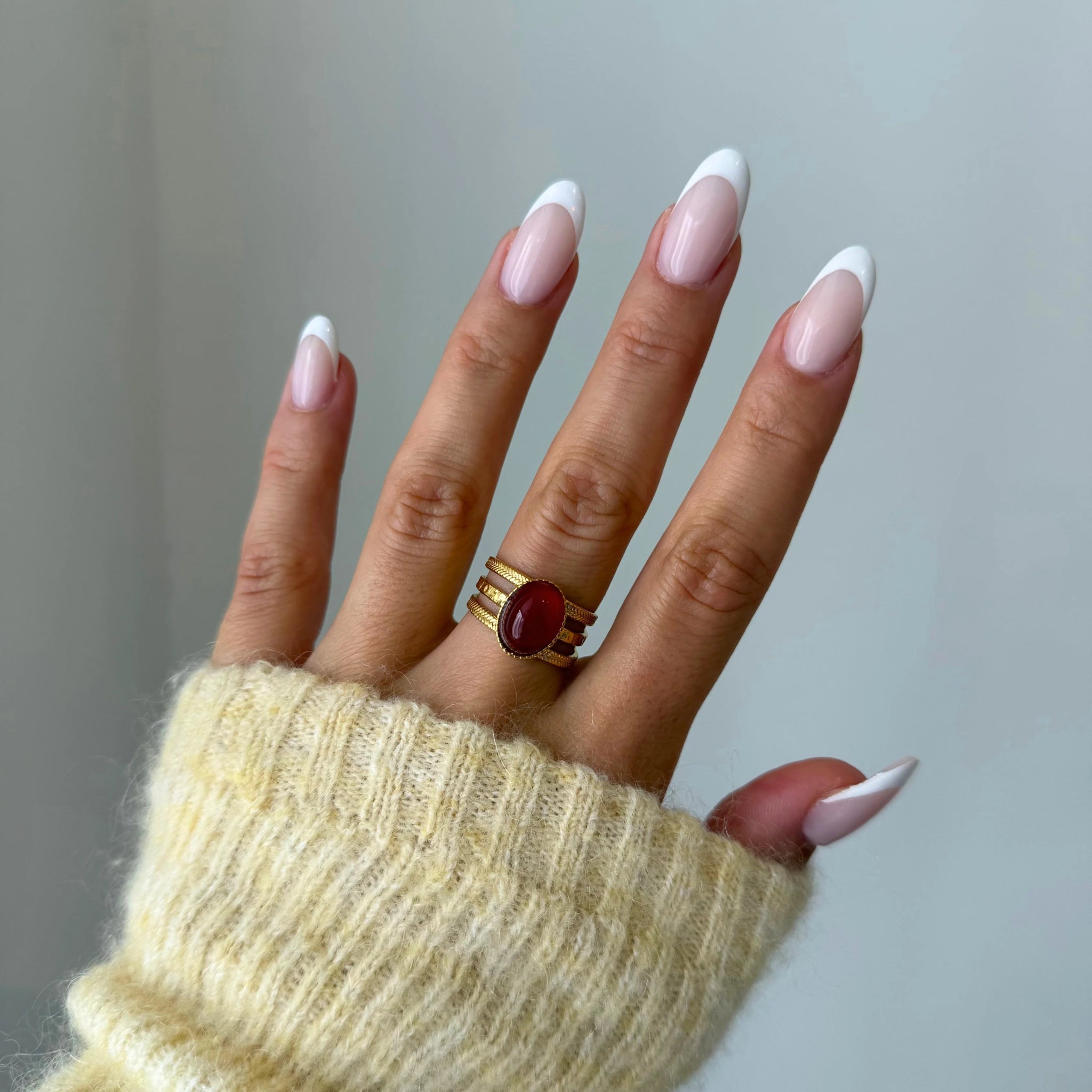Bague Rubia style vintage avec pierre rouge portée sur une main avec manche en maille jaune.