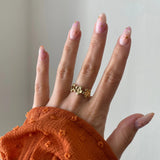 Gros plan bague Sandra motif couronne de fleurs portée au doigt, style romantique et printanier.