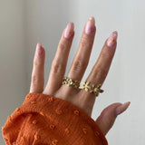 Bague fleurie Sandra portée en accumulation (stacking) avec une bague statement dorée sur une main avec manche rouille.