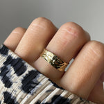 Gros plan bague dorée texturée effet froissé portée au doigt.