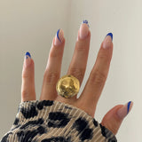 Gros plan bague Tatiana forme pastille XXL ou médaille bombée portée au doigt, style statement affirmé.