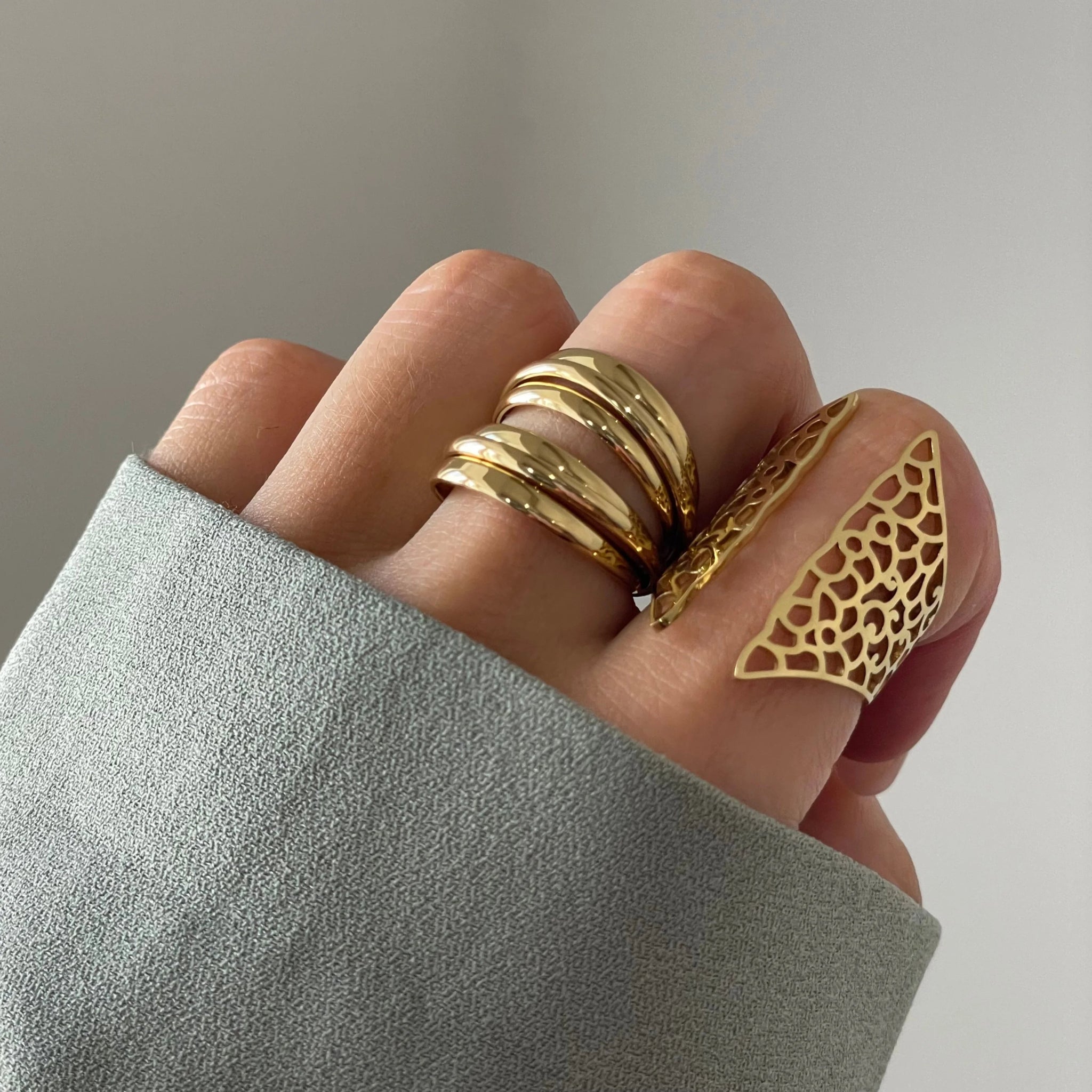 Bague Teresa portée en accumulation avec une bague bouclier filigrane sur une main avec manche grise.