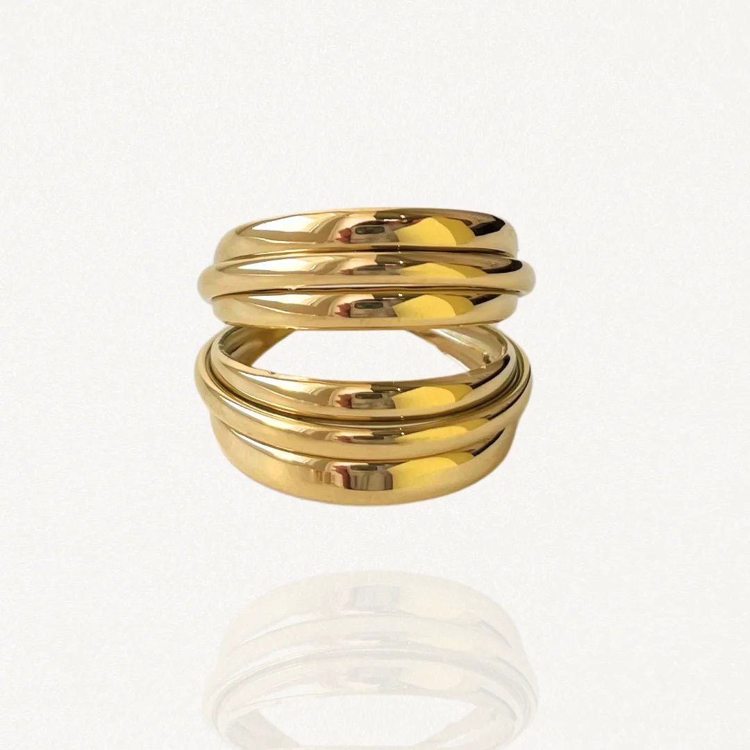 Bague large multi-rangs effet empilé en acier inoxydable doré au design sculptural et enveloppant sur fond blanc.