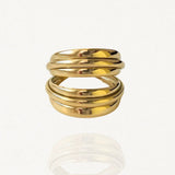 Bague large multi-rangs effet empilé en acier inoxydable doré au design sculptural et enveloppant sur fond blanc.