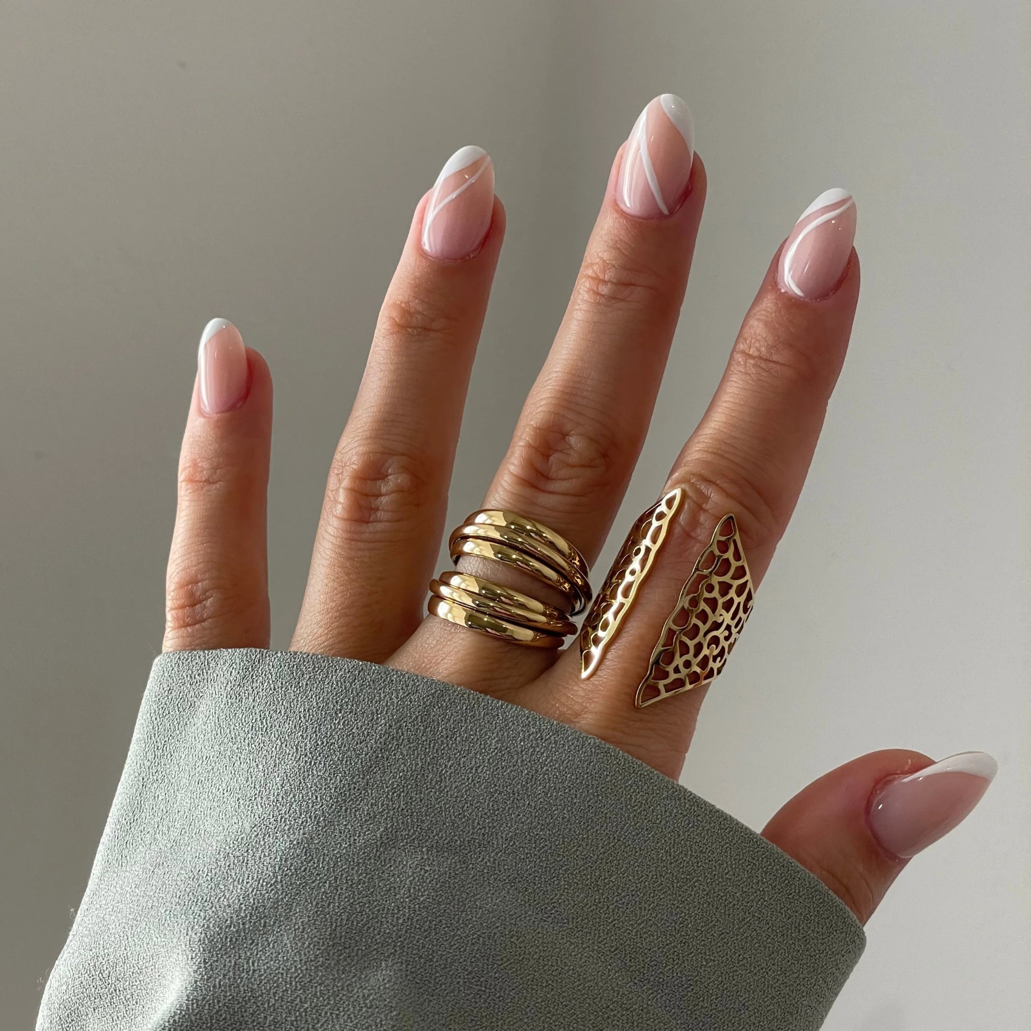 Bague Teresa portée en accumulation avec une bague bouclier filigrane sur une main avec manche grise.