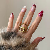 Main de femme portant une bague dorée motif tourbillon, mettant en valeur un style chic et moderne.