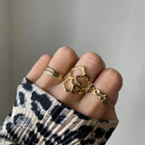 Bague fine double rang Ursula portée en accumulation avec d'autres bagues graphiques dorées sur une main avec pull léopard.