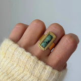Gros plan bague Veronika style vintage avec pierre rectangulaire verte portée au doigt, accessoire bohème chic.