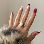 Bague style vintage avec pierre blanche ovale portée par une femme avec un manteau en fausse fourrure et des ongles nails art.