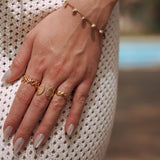 Trois bagues en acier inoxydable doré avec motifs coquillages et étoile de mer sur une main de femme.