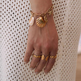 Trois bagues en acier inoxydable doré, motifs coquillages et épines, sur main de femme.