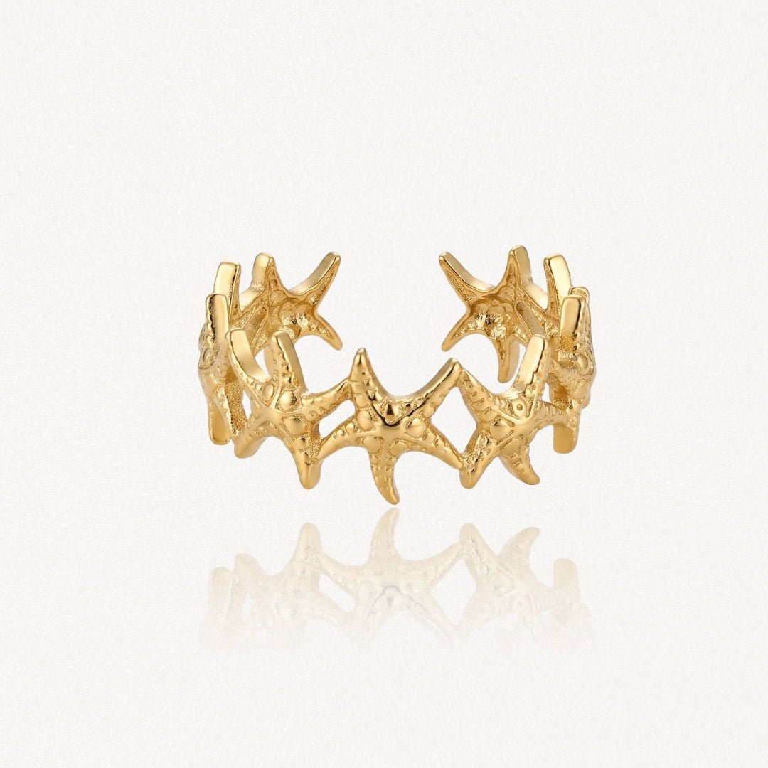 Bague ajustable en acier inoxydable doré, ornée de multiples étoiles de mer texturées formant une bande.