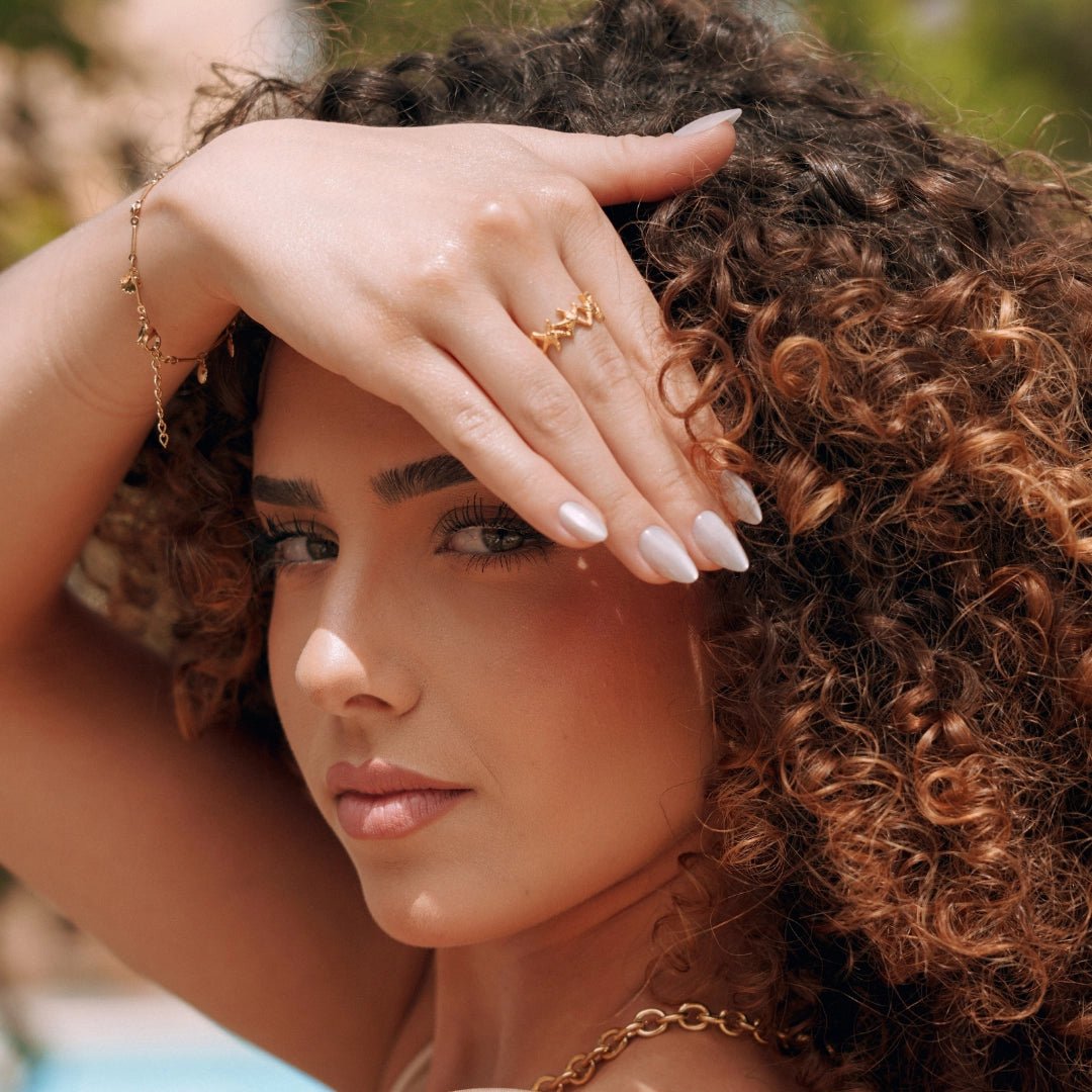 Bague en acier inoxydable doré à motif de chevrons ajourés, portée sur la main d'une femme aux cheveux bouclés.