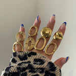 Bagues graphiques portées en accumulation avec d'autres bagues dorées sur une main avec pull léopard.