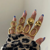 Bagues graphiques portées en accumulation avec d'autres bagues dorées sur une main avec pull léopard.
