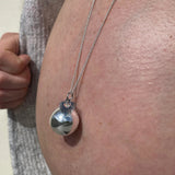 Bola de grossesse argenté porté sur le ventre rond d'une femme enceinte, bijou de maternité apaisant.