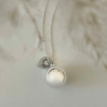 Bola de grossesse en acier inoxydable argenté avec pendentif sonore et breloque cœur sacré rayonnant sur fond blanc.