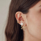 Boucles d'oreilles fleur acien inoxydable doré et blanc avec manchette assortie, portées sur l'oreille d'une femme.