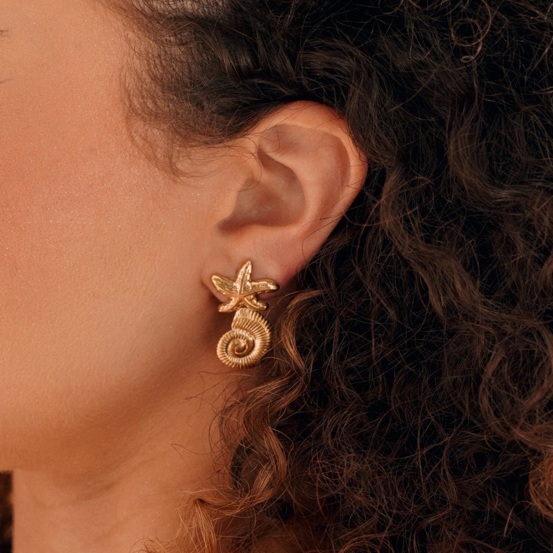 Boucles d'oreilles en acier inoxydable couleur or: étoile de mer fixée à un coquillage en spirale, sur l'oreille.