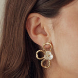 Boucles d'oreilles fleur en acier inoxydable doré martelé, centre nacré, portées sur l'oreille d'une femme.