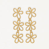 Boucles d'oreilles pendantes en acier inoxydable doré, motif 3 fleurs stylisées reliées, fond blanc.