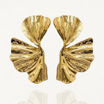 Paire de boucles d'oreilles larges motif abstrait feuille plissée dorée sur fond blanc.