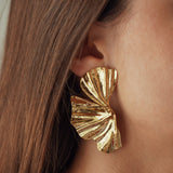 Boucles d'oreilles statement grand format forme feuille de Ginkgo plissée ou éventail en acier inoxydable doré portées.