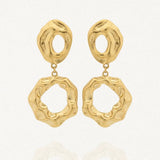 Une paire de boucles d'oreilles dorées Arlette en acier inoxydable. Chaque boucle est formée de deux éléments asymétriques et texturés, reliés par un petit anneau, sur un fond blanc avec une légère réflexion.