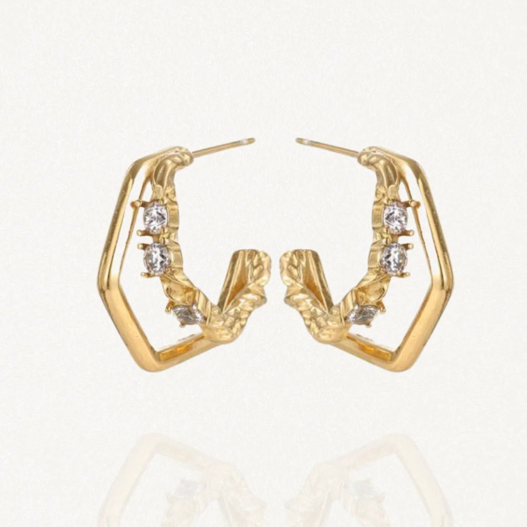 Paire de créoles géométriques (forme hexagonale) en acier inoxydable doré ornées de petits cristaux et détails texturés sur fond blanc.