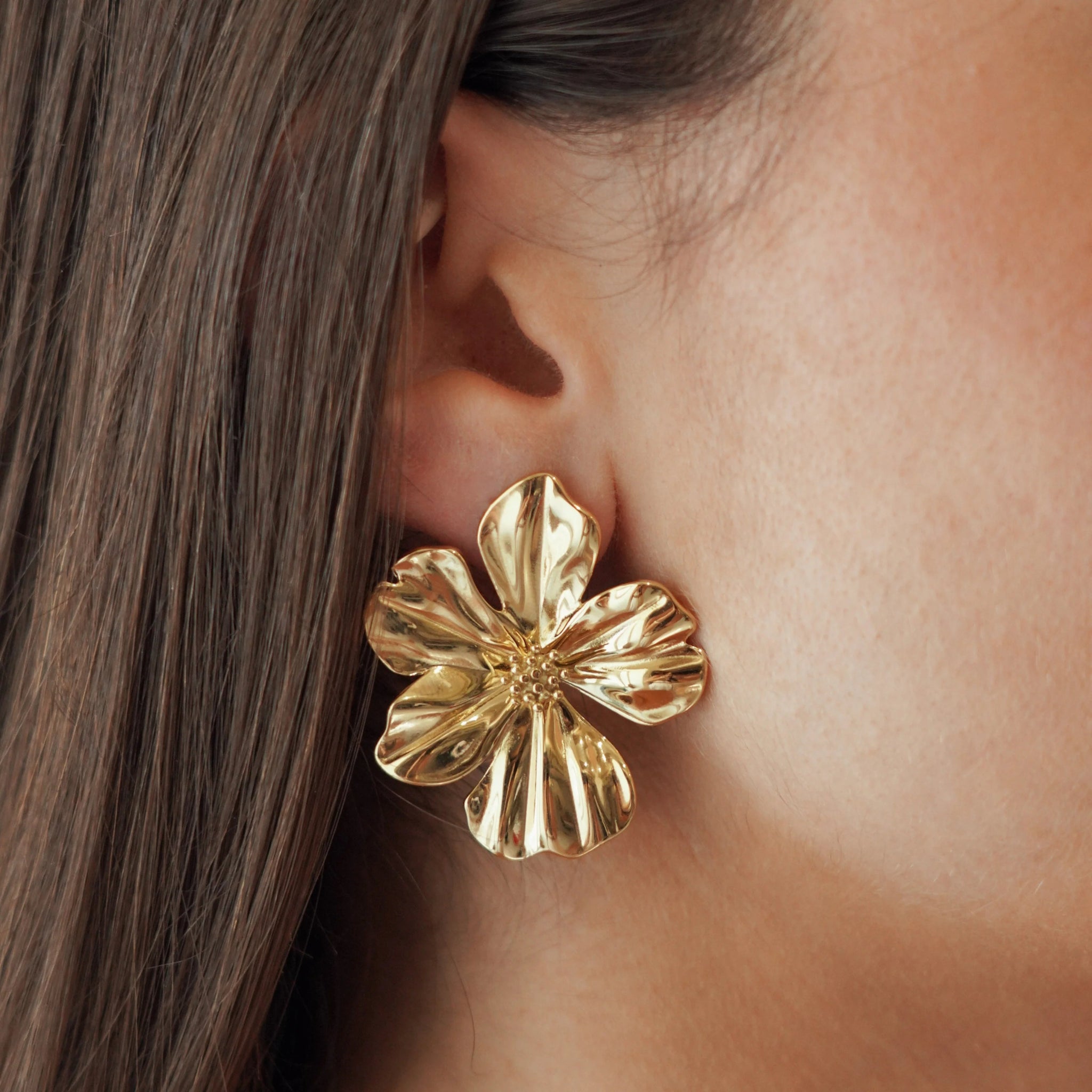 Boucles d'oreilles grand format forme fleur épanouie en acier inoxydable doré portées à l'oreille, style statement.